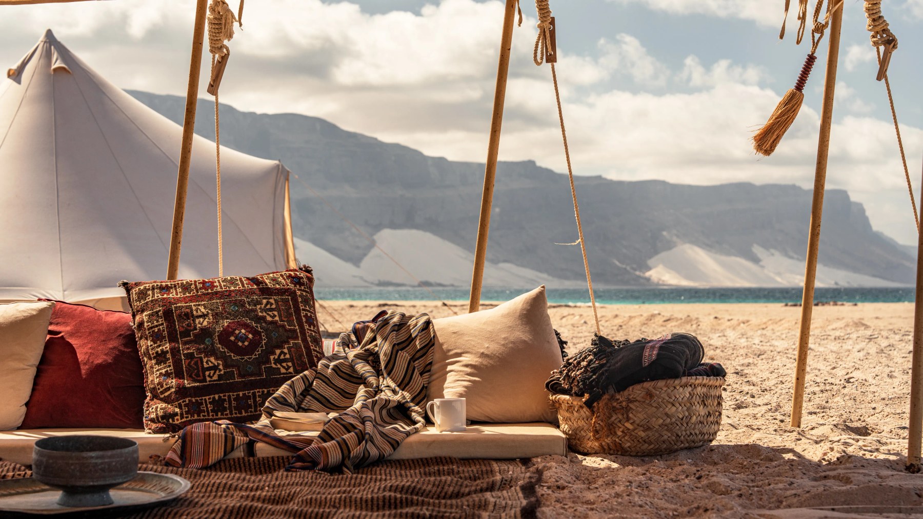 Woven cushions and a blanket in a beachside tent, mountains beyond